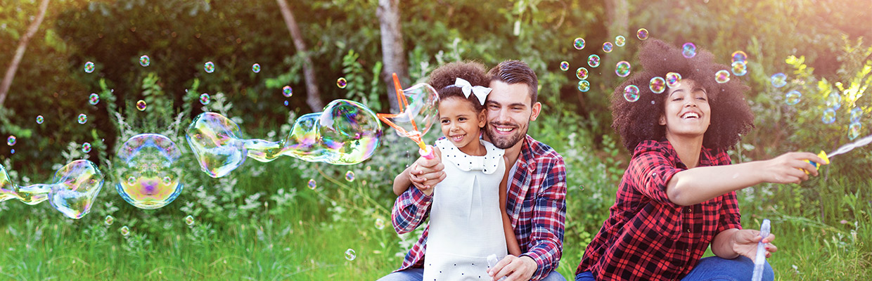 a happy family of three playing soap bubbles in the woods; image used for HSBC Mauritius accounts page